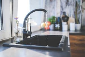 Close-up photo of a kitchen sink with a single-handled faucet stuck in the "on" position, water flowing from the spout. This image depicts a situation where you might need to follow a guide on how to remove a stuck tap handle.