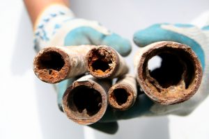 A person wearing gloves holding up multiple corroded and clogged pipes, illustrating the severity of plumbing issues. This image can be used to emphasize the importance of knowing how to unclog a toilet without a plunger as part of a comprehensive guide.