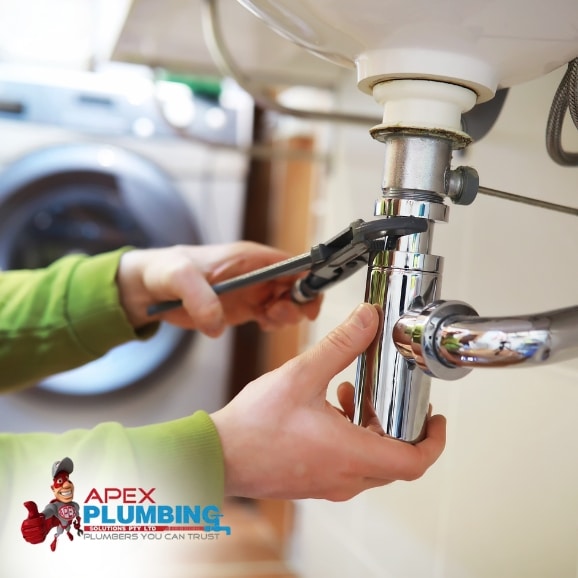 Burst Pipe Repairs: A plumber is using a wrench to fix a leaking pipe under a sink.