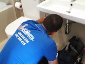 Professional plumber fixing a slow draining sink issue under a bathroom sink for proper water flow.