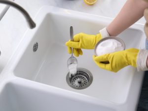 Hands in yellow gloves using baking soda to fix a sink that won't drain, showing a DIY unclogging method.