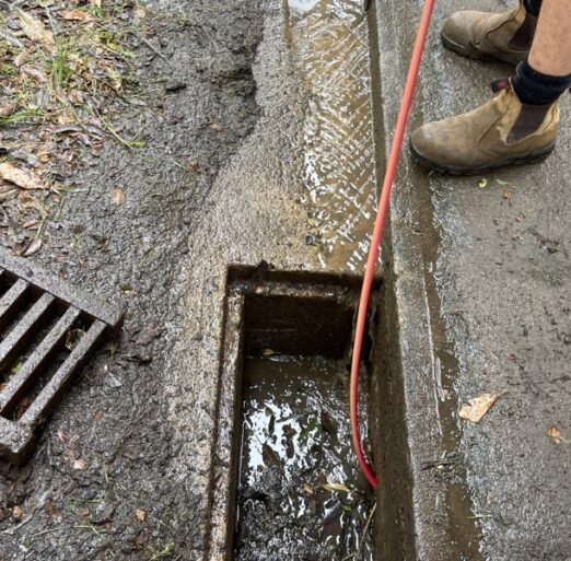 A professional plumber clearing tree roots in drainage pipes with specialised tools near a stormwater drain.