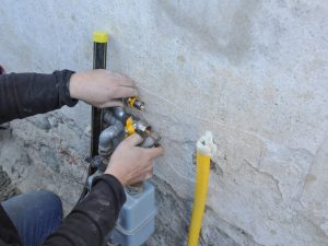 Close-up of a worker fixing a faulty gas meter with visible pipes and a yellow hose.