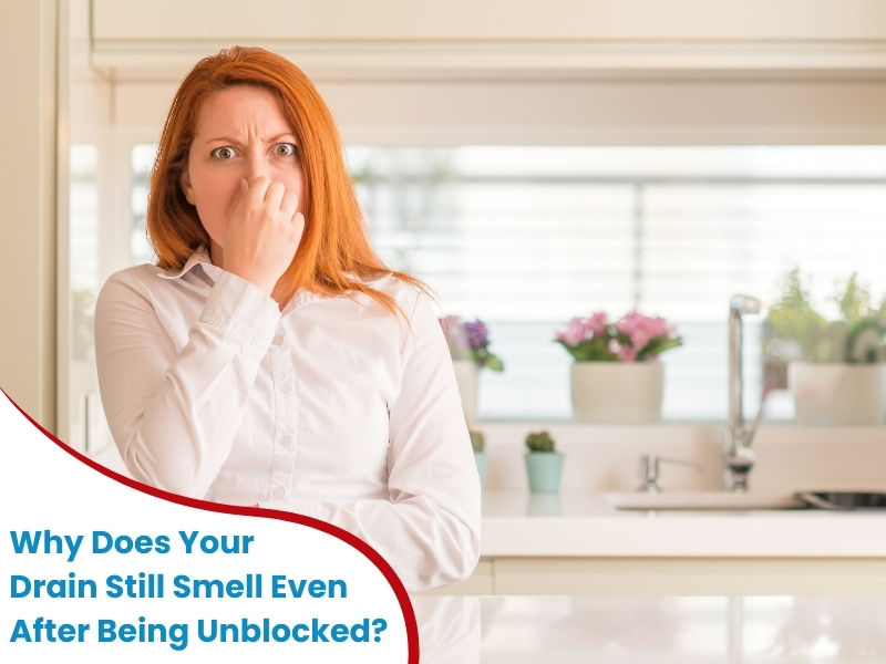 Frustrated woman in a kitchen holding her nose due to a smelly drain even after unblocking efforts.