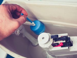 A hand adjusts a toilet tank fill valve to address a possible toilet tank overflow.