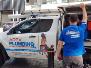 A plumber standing next to an Apex Plumbing service vehicle, ready to repair rusting pipes in residential and commercial properties.