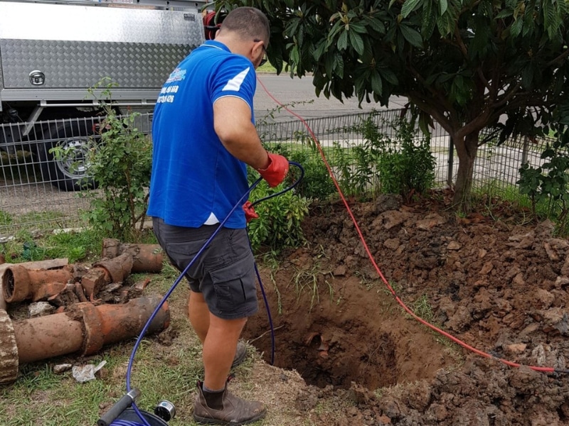 Plumber inspecting underground pipes in a backyard to diagnose emergency plumbing problems with CCTV drain inspection equipment.