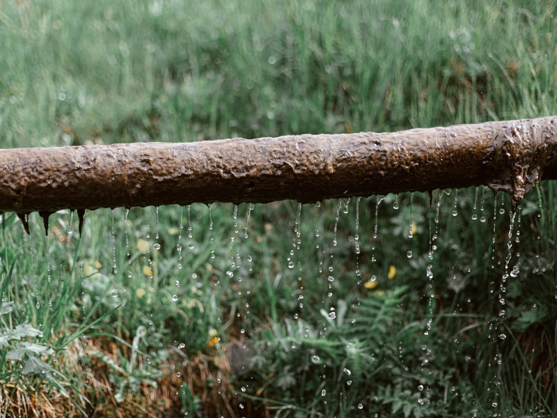 Corroded metal pipe leaking water outdoors while clearing drain blockages