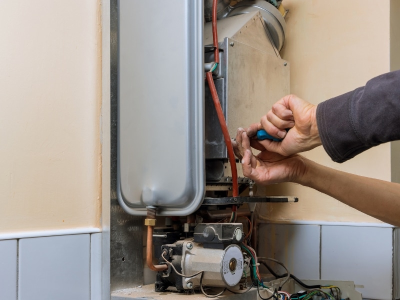 Technician repairing a gas instant hot water system inside a home