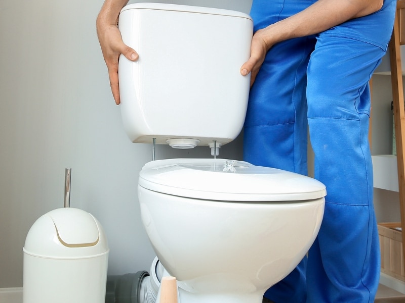 Plumber lifting toilet tank to repair leaking toilet tank