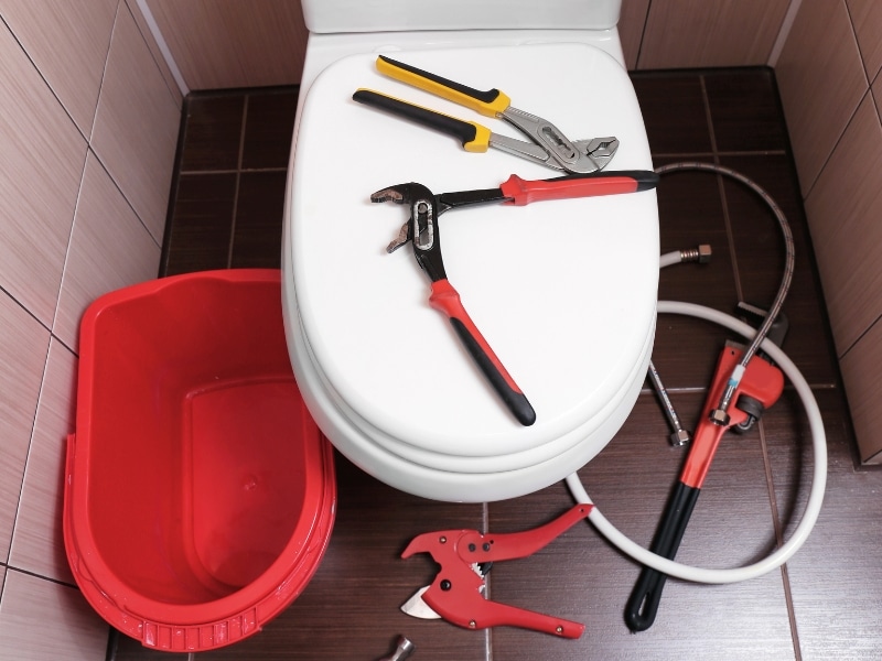 Tools and bucket ready to stop leaky toilet repair on bathroom floor.