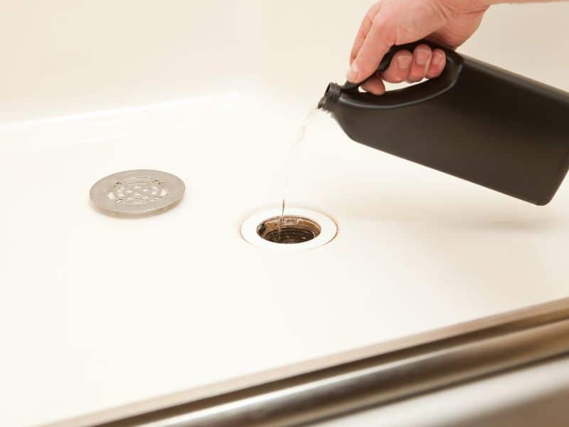 Person pouring drain cleaner into sink for clearing a blocked drain.