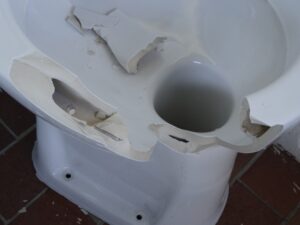 Broken toilet base showing cracks and exposed porcelain after failed attempt to repair flange toilet connection.