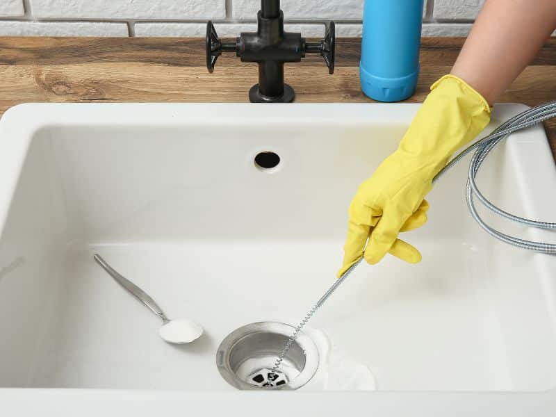 Person using a plumbing snake for clearing a blocked drain in kitchen sink.