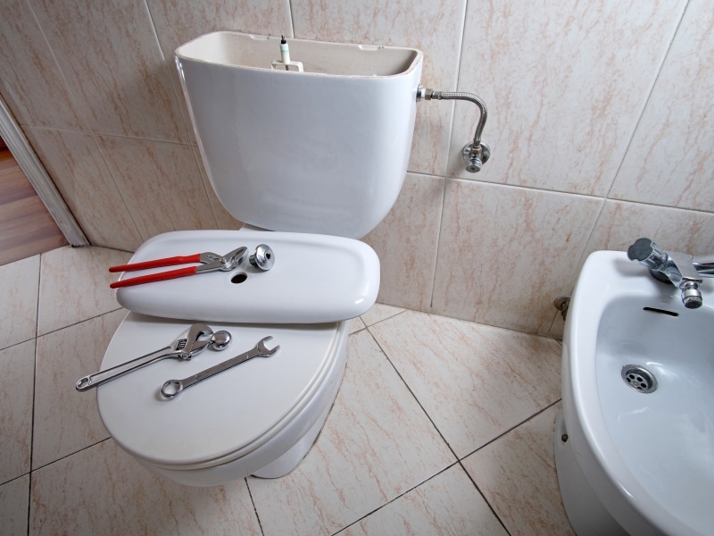 Open cistern and tools used to stop leaky toilet in bathroom