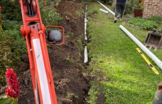 Excavation trench in a backyard with new PVC piping and machinery during a Blocked Drain replacement and repair.
