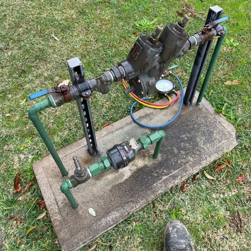 Technician servicing a backflow prevention device beside a water meter in garden