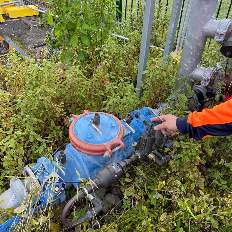 Technician servicing a backflow prevention device beside a water meter in garden