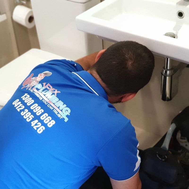 Plumber inspecting an active leak under a bathroom vanity during leaking tap repair