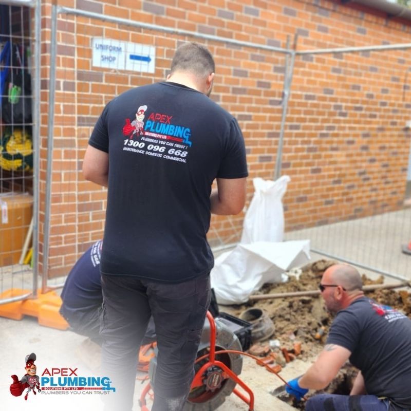 Apex plumbers clearing a stormwater pit during excavation beside a brick building