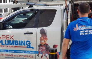 A licensed plumber unloading tools from an Apex Plumbing service ute on a city street, representing a professional Plumber Sydney.