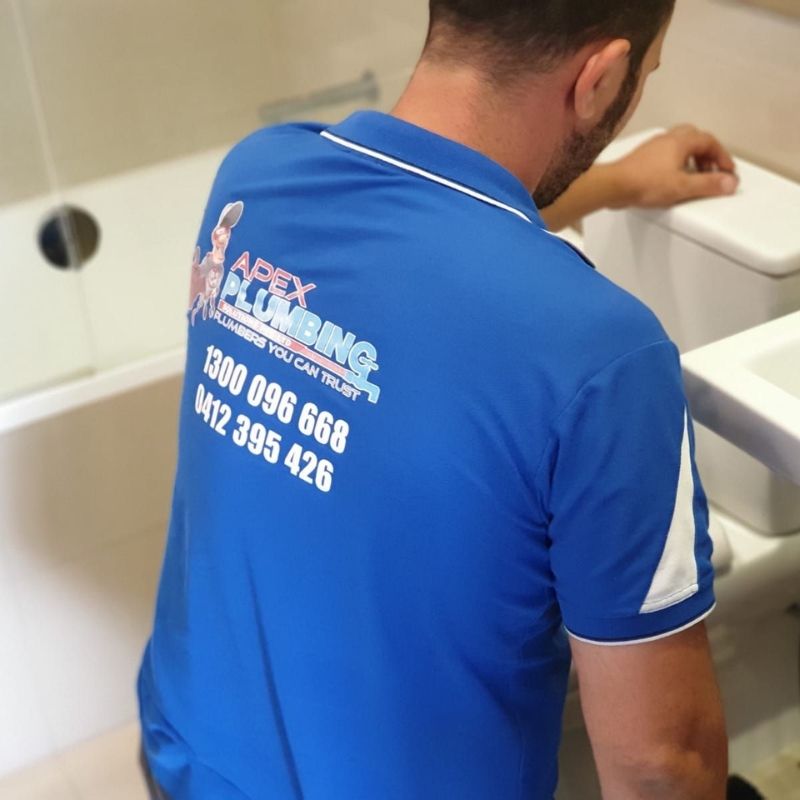 Plumber inspecting a toilet cistern in bathroom during a toilet repair.