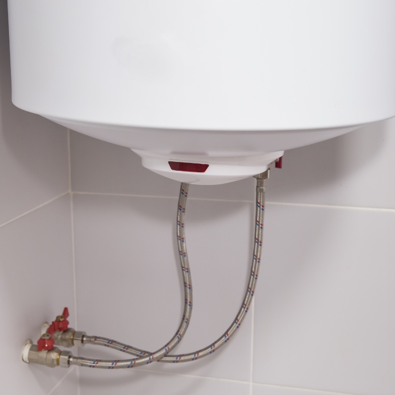 Close-up of a modern wall-mounted hot water system showing the bottom base, flexible braided hoses, and valves.