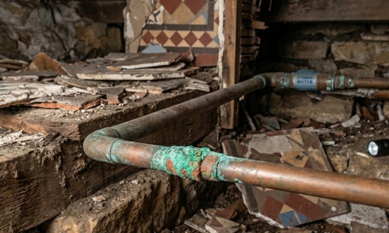 Plumber checking corroded copper water pipe beneath an older Sydney terrace bathroom floor.